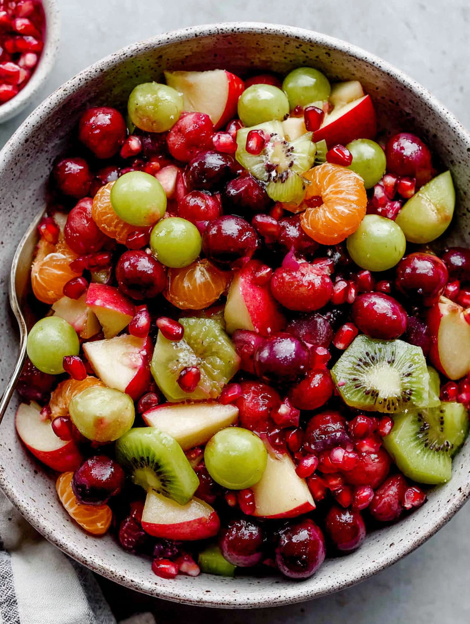 A bowl of fruit salad with kiwi, apples, and oranges.
