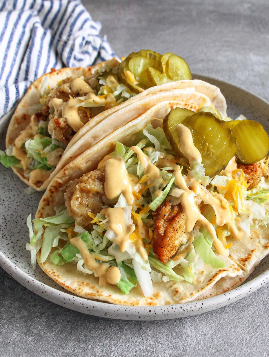 A plate of food with two tacos and pickles.