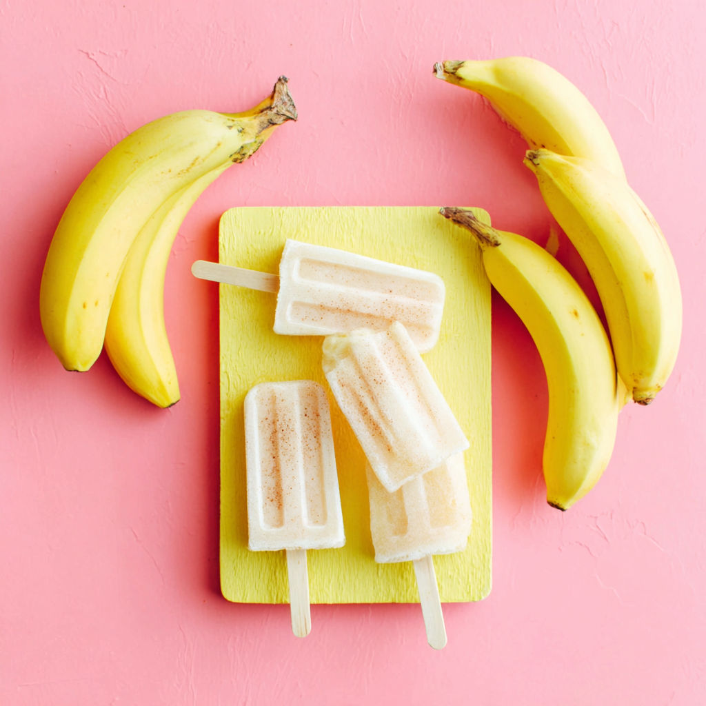 Three banana popsicles on a yellow board.