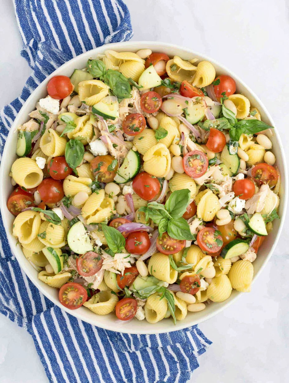 A bowl of pasta salad with tomatoes, cucumbers, beans, and spinach.