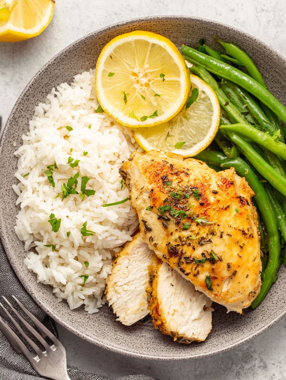 A plate of food with rice, chicken, green beans, and lemon wedges.