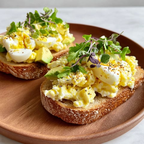 Two pieces of toast with egg salad and cottage cheese on top.