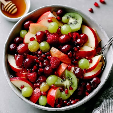 A bowl of fruit salad with kiwi, grapes, apples, and pomegranates.