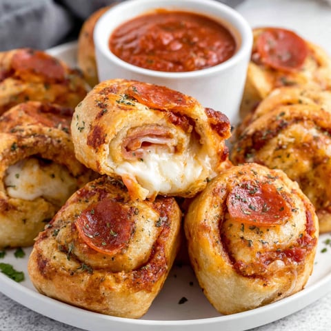 A plate of pepperoni pizza rolls with a bowl of sauce.