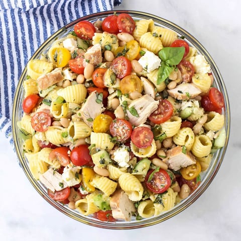 A bowl of pasta salad with chicken, tomatoes, beans, and cheese.