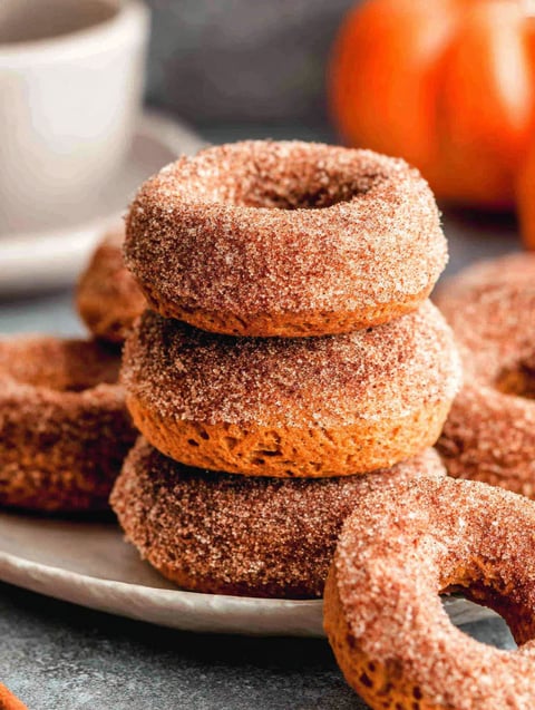 Pumpkin spice baked donuts stacked on a plate.