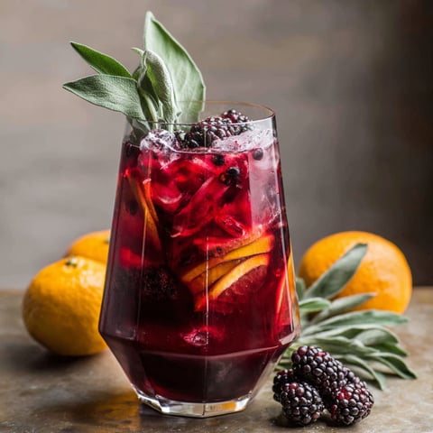 A glass of red wine with blackberries and sage.
