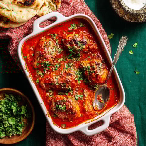 A dish of baked butter chicken with green herbs on top.
