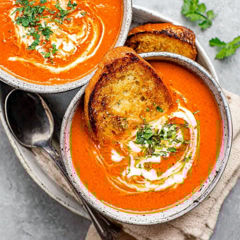 A bowl of tomato bisque with a spoon in it.
