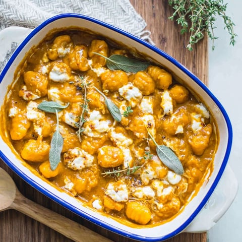 A bowl of pumpkin gnocchi bake with white cheese on top.