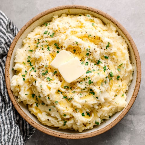 A bowl of mashed potatoes with a pat of butter on top.