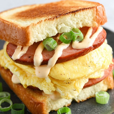 A breakfast sandwich with eggs, sausage, and mustard.